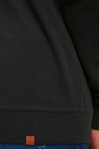 Black sweatshirt featuring ribbed hem, soft texture, and a small brown leather label at the bottom left.