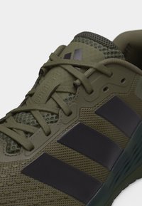 Chaussure de sport vert olive avec des rayures noires, tissu en maille, lacets noués et "DROPSET" embossé près de la languette rembourrée.