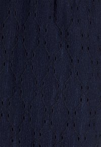 Tmavě modrá texturovaná látka se vzorem diamantů a malými výřezy, které vytvářejí jemný kontrast a přidávají hloubku celkovému designu.