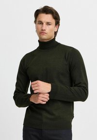 Pull à col roulé vert foncé avec manches longues et poignets côtelés. Fabriqué dans un tissu doux, il présente une coupe décontractée et une texture subtile.