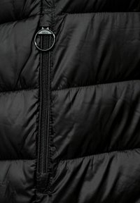 Black padded jacket featuring a central zipper, round pull tab with "CECIL" branding, and quilted texture.