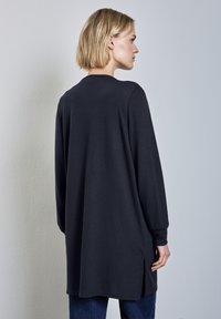 Mörkgrå långärmad tunika i mjukt tyg, med sidoslitsar och avslappnad passform, matchad med blå jeans.