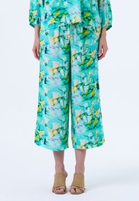 Heldere turquoise en groene bloemenprint op lichtgewicht stof, met loszittende, cropped broeken gecombineerd met geweven beige hakken.