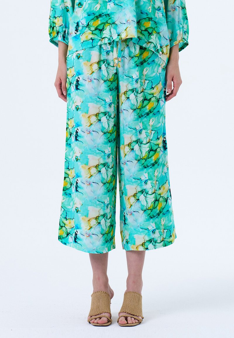 Heldere turquoise en groene bloemenprint op lichtgewicht stof, met loszittende, cropped broeken gecombineerd met geweven beige hakken.