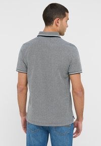 Szary polo z teksturowanym wykończeniem, z klasycznym kołnierzykiem w granatowym kolorze i krótkimi rękawami, w parze z niebieskimi dżinsami.