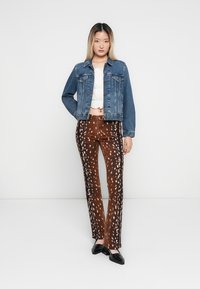 Jachetă din denim cu un design ajustat, asortată cu pantaloni maronii cu un model cu pete. Un top texturat alb completează ținuta. Sunt purtate pantofi negri.