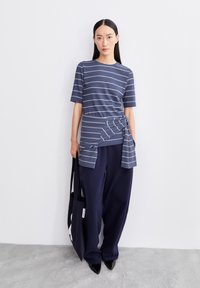 Navy gestreepte t-shirt met een knoopdetail in de taille, gecombineerd met navy wijde broek en een zwarte totebag. Gladde stof en losse pasvorm.