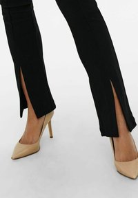 Svarta tajta byxor med sprund på fållen, kombinerade med beige stilettklackar. Tyget verkar ha en texturerad och elastisk känsla.