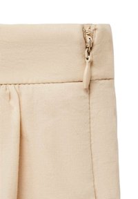 Sezione di pantaloni in tessuto beige con zip nascosta e texture morbida; presenta pieghe ordinate e una vita liscia.