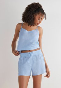Lichtblauw gestreept slaapset bestaande uit een mouwloos bovenstuk met v-hals en bijpassende shorts met elastische taille en trekkoord.