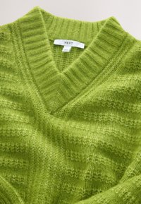 Pull en maille verte douce à col en V avec col côtelé, montrant la texture et une étiquette de la marque « NEXT » à l'intérieur de l'encolure.