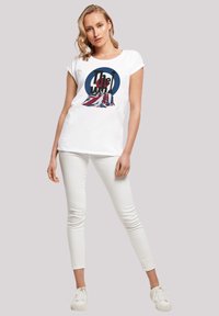 White cotton t-shirt featuring a round graphic in blue and red with the text "The Who" and a Union Jack design. Paired with white pants and sneakers.