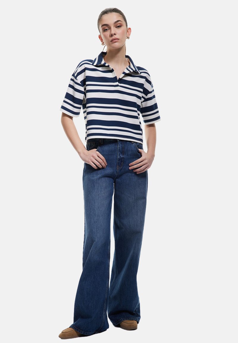 Polo a righe blu navy e bianche con colletto, abbinato a jeans blu a vita alta e gamba larga. Dettagli in tessuto testurizzato visibili.