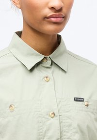 Κοντινό πλάνο ενός ατόμου που φοράει πουκάμισο ανοιχτού πράσινου χρώματος με κουμπιά και γιακά και μικρό λογότυπο Columbia στην τσέπη του στήθους.