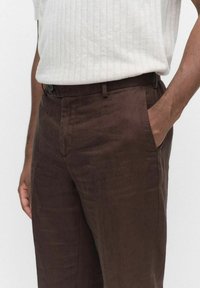 Bruna linbyxor med en slät textur, löst snitt och framfickor. Midjan har ett bälteshål och en knappstängning.