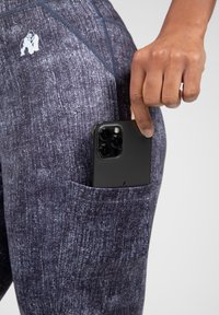 Rekbare leggings van een gestructureerde donkergrijze stof, met een zijzak die een zwarte smartphone bevat. Klein logo op de taille.