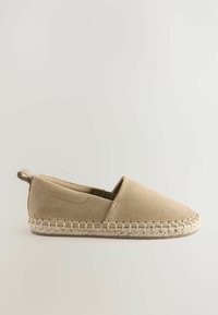 Espadrille beige con parte superior de ante y lados elásticos. Presenta una suela de yute trenzado y una pequeña pestaña en el talón.
