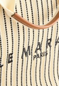 Vävd beige väska med svarta ränder och präglad text "LE MARAIS PARIS"; har ett handtag i beige läder med synliga stygn.