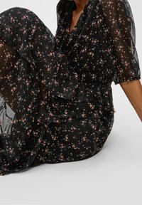 Svart blommig klänning med korta ballongsärmar, tillverkad av genomskinligt material prytt med små rosa och blå blommor, med midja som är figurnära.