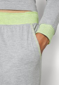 Grijze sweatshirt met geribbelde neon groene accenten op de halslijn en mouwen. Bevat een zijzak en zachte, gestructureerde stof.