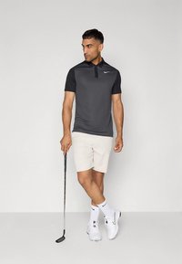 Nike pikétröja i mörkgrått med korta ärmar och krage, kombinerad med ljusbeige shorts. Outfitten kompletteras med vita golfskor.