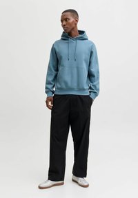 Světle modrá mikina s kapucí, přední kapsou, stahovacími šňůrkami a žebrovanými manžetami, v kombinaci s černými širokými kalhotami a botami se stříbrnými akcenty.