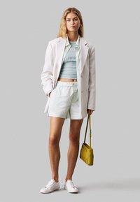 Blazer blanco, top corto acanalado azul claro, pantalones cortos rayados en blanco y menta. Accesorios: bolsa amarilla y zapatillas blancas. Texturas suaves, ajuste casual.
