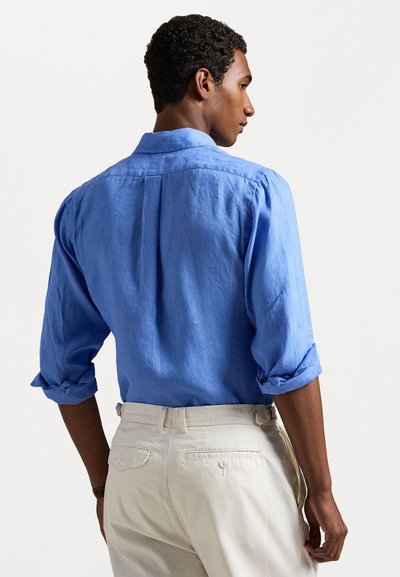 Lys blå lin skjorte med oppbrettede ermer, bakfold og standard krage, kombinert med kremfargede bukser.