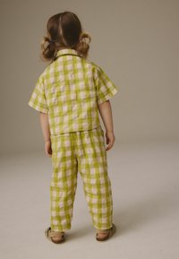 Chemise en coton à carreaux verts et blancs avec des manches courtes et un pantalon assorti, présentant une coupe décontractée et des chaussures simples et plates.