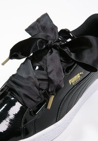 Baskets Puma Basket noires vernies avec de larges lacets en ruban de satin noir et une semelle blanche texturée sur fond blanc.