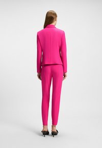 Costume rose vif avec blazer ajusté et pantalons slim. Tissu lisse avec un design sur mesure, présentant un col classique et des coutures simples.