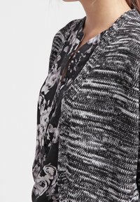 Black and white patterned top with floral design, textured knit material, and a v-neckline. Features a layered, asymmetrical look.