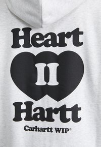 Hoodie grigio chiaro con una grafica nera audace con il testo "Heart II Hartt" e una forma a cuore, realizzato in tessuto morbido con una finitura texturizzata.