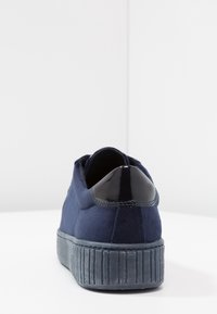 Námořnické semišové tenisky s lesklým černým patentním koženým podpatkem a strukturovanou gumovou podrážkou s vertikálními drážkami.