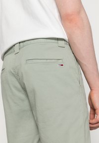 Shorts en coton vert clair avec deux poches arrière. Présente un petit détail de logo rouge, blanc et bleu près de la poche droite. Design simple et épur é.