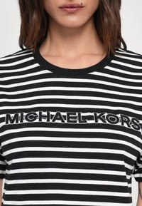 Svart og hvit stripete t-skjorte med brodert "MICHAEL KORS" tekst over brystet. Korte ermer, rund hals design.