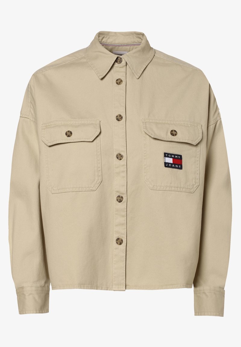 Chemise beige boutonnée à manches longues, deux poches avant à rabat et un écusson avec le logo Tommy Jeans sur la poche droite.