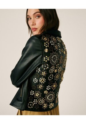 Mujer con cabello oscuro que lleva una chaqueta de cuero negra decorada con tachuelas doradas y plateadas en patrones florales circulares en la espalda.
