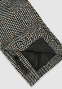 Pilkos ir juodos spalvų šuns danties rašto kelnės su rudais languotais akcentais. Juosmuo puošiamas keturiomis juodomis sagomis, o paslėptame kišenės viduje yra juodas pamušalas.