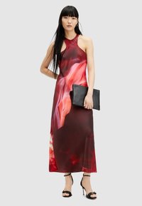 Maxi dress in red and pink abstract print, halter neckline, fitted bodice, flowing fabric. Model holds a black clutch and wears black heels.