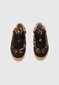 Par de zapatillas con cordones con estampado de leopardo y acentos de ante marrón oscuro, forro interior beige y suelas marrón claro sobre un fondo neutro.