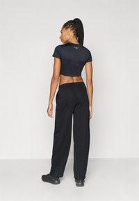 Μαύρο κοντοκομμένο μπλουζάκι με κοντά μανίκια και λογότυπο στο πίσω μέρος, συνδυασμένο με μαύρη άνετη φόρμα και μαύρα παπούτσια.