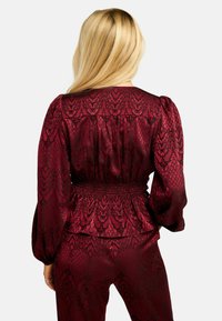 Burgundi siidist pluus smokitud vöökoha, tekstuurse lillemustri, mahukate pikkade varrukate ja ümarate kaelusega.