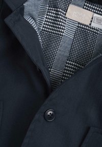 Veste marine avec un col cranté, dotée d'une fermeture à boutons et d'une doublure à carreaux dans des tons de bleu et blanc avec des motifs géométriques.