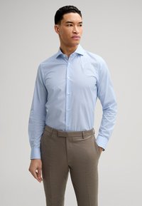 Chemise à manches longues bleu clair avec des points en motif subtil, associée à un pantalon beige. Tissu texturé et design de col classique.