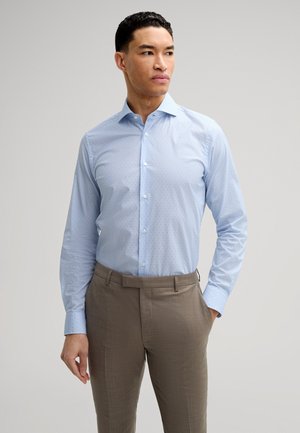 Camicetta azzurro chiaro a maniche lunghe con piccoli punti a motivo, abbinata a pantaloni beige. Tessuto strutturato e design del colletto classico.