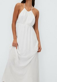 Weißes Neckholderkleid mit gerafftem Ausschnitt, fließender Silhouette und weicher Textur, reicht bis zur Mitte der Wade und zeigt eine schlichte Gestaltung.