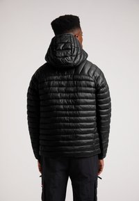 Giubbotto imbottito nero con un design a trapunta e cappuccio, caratterizzato da linee orizzontali e una texture liscia. Cuciture visibili sulle giunture.