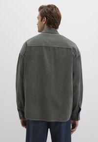Grüne Cordhemd mit entspannter Passform, Knopfriegelärmeln und horizontaler Rippstruktur. Der Rücken verfügt über eine Schulternaht und einen geraden Saum.