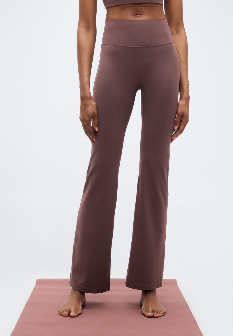 Φαρδύ κολάν σε ζεστή καφέ απόχρωση, κατασκευασμένο από απαλό ύφασμα με ψηλή μέση και χωρίς ορατές ραφές, παρουσιασμένο πάνω σε υφασμάτινο χαλάκι.